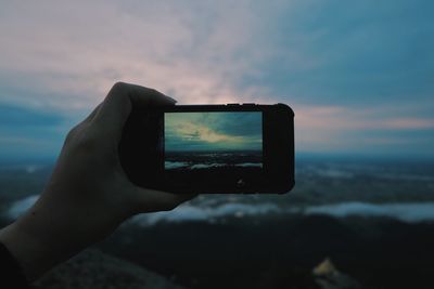 Close-up of hand holding smart phone against sky