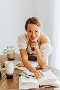 Woman with a recipe book looking at camera while cooking at kitchen