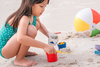 Side view of cute girl in swimwear playing with toys on beach