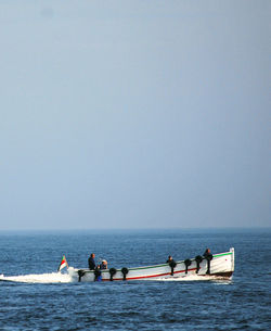 Men on boat in sea against clear sky