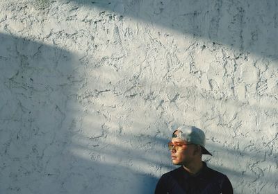 Man looking away while standing against wall