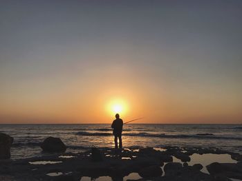 Silhouette man finshing on beach against sky during sunset