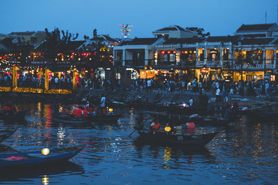 Boats in canal by illuminated buildings at dusk