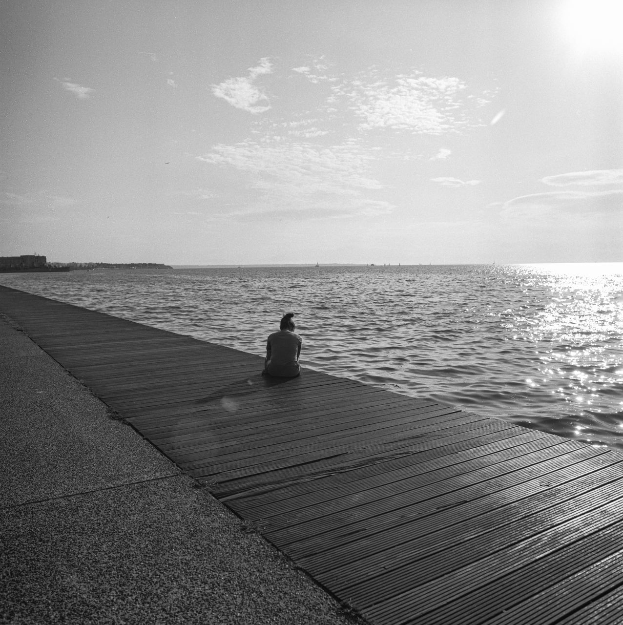 water, sea, sky, sitting, horizon, one person, real people, leisure activity, scenics - nature, lifestyles, tranquil scene, beauty in nature, horizon over water, tranquility, nature, rear view, day, relaxation, outdoors, promenade, looking at view