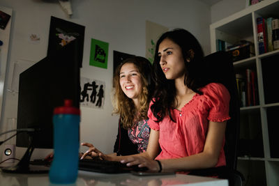 Happy teenage girl using computer with friend in darkroom at home