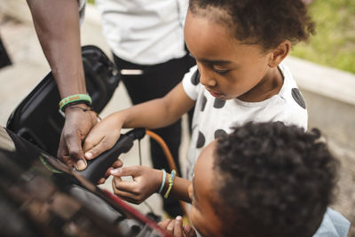 Midsection of father assisting children in charging car on driveway