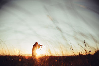 Man aiming rifle on field against sky