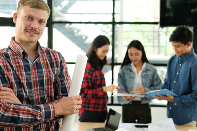 Portrait of confident male architect holding blueprint while standing in office