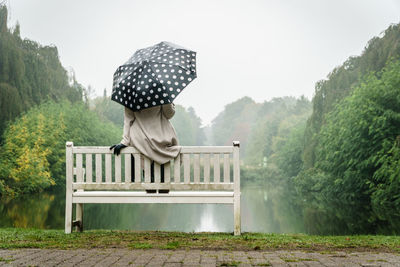 Rear view of woman with umbrella on field sitting in an bench