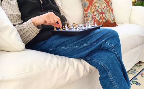 Midsection of man playing chess while sitting on sofa at home