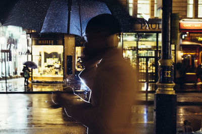 Side view of man standing in wet illuminated city at night