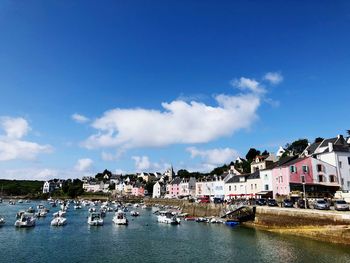 Sailboats moored in sea by townscape against blue sky