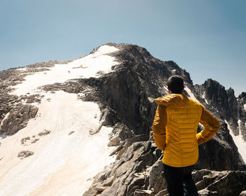 Rear view of man walking on snowcapped mountain against sky