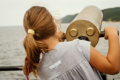 Girl looking through coin-operated binoculars against sea