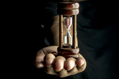 Midsection of person holding hourglass against black background