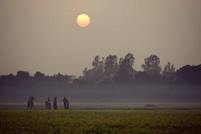 People on field against clear sky during sunset