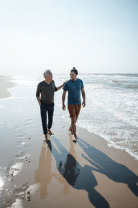 Father walking with son near seashore at beach on sunny day