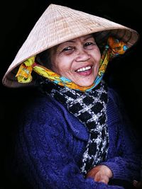 Portrait of smiling senior woman wearing asian style conical hat against black background