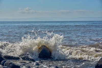 Sea waves splashing on shore against sky