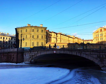 Bridge over river by buildings against sky in city