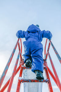 Rear view of boy on slide against sky during winter