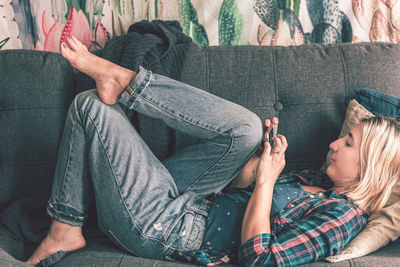 Side view of woman using smart phone while lying on sofa at home