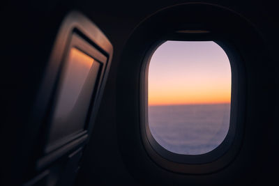 Window of airplane during flight above clouds at beautiful sunset.