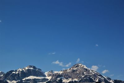 Low angle view of snowcapped mountains against blue sky