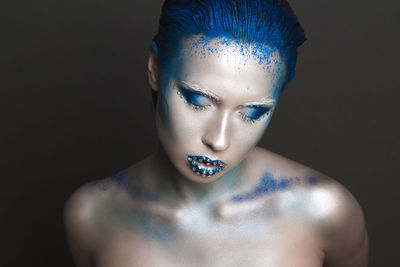 Close-up of woman with eyes closed wearing make-up against black background