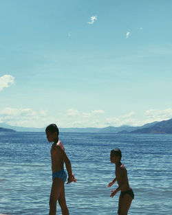 Rear view of friends on sea shore against sky