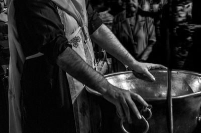 Midsection of priest standing by container during baptism at church