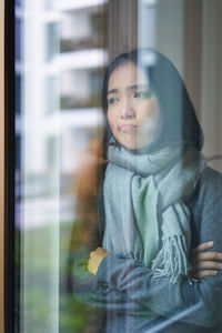 Portrait of young woman looking through window