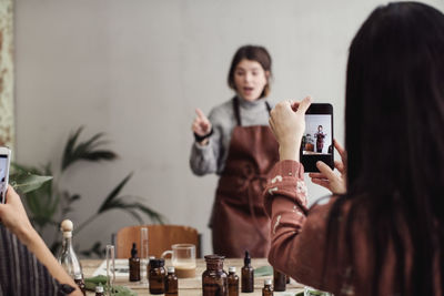 Female colleagues photographing mid adult owner explaining at perfume workshop