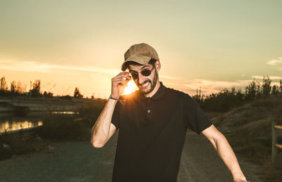 Portrait of young man wearing sunglasses while standing against sky during sunset