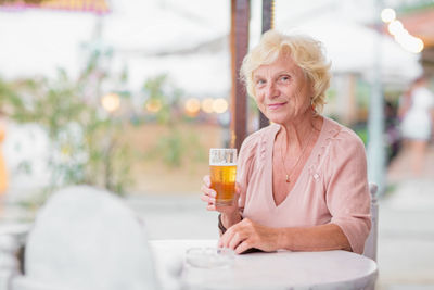 Mature woman sitting at a table in a summer cafe and drinking beer