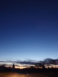 Silhouette trees on field against clear blue sky