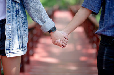 Midsection of couple holding hands on footbridge