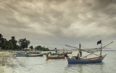 Boats in harbor against cloudy sky