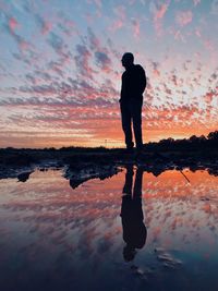 Silhouette man standing on shore against sky during sunset