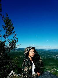 Portrait of young woman standing against blue sky