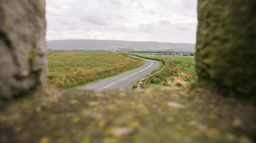 Surface level of road amidst field against sky