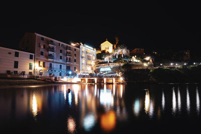 Illuminated buildings by river against sky at night