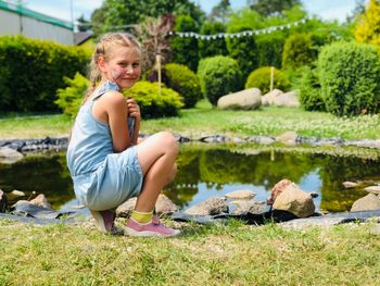 Portrait of smiling cute girl crouching by pond