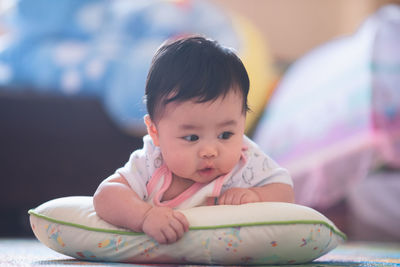 Cute baby girl leaning on cushion at home