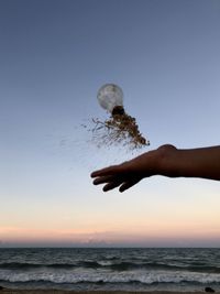 Cropped hand throwing light bulb over sea