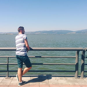 Man standing on railing by sea against clear sky