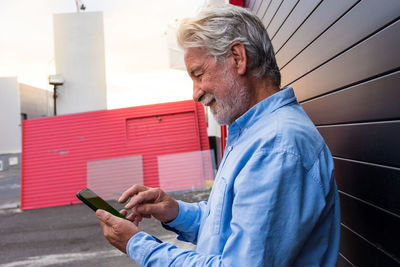 Side view of senior man using mobile phone outdoors