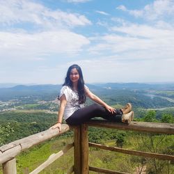 Portrait of smiling woman sitting on railing against sky