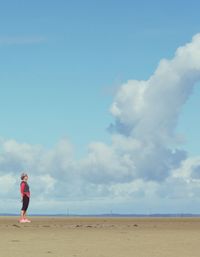 Side view of woman standing at beach against cloudy sky