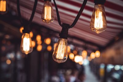 Close-up of illuminated light bulb hanging from ceiling